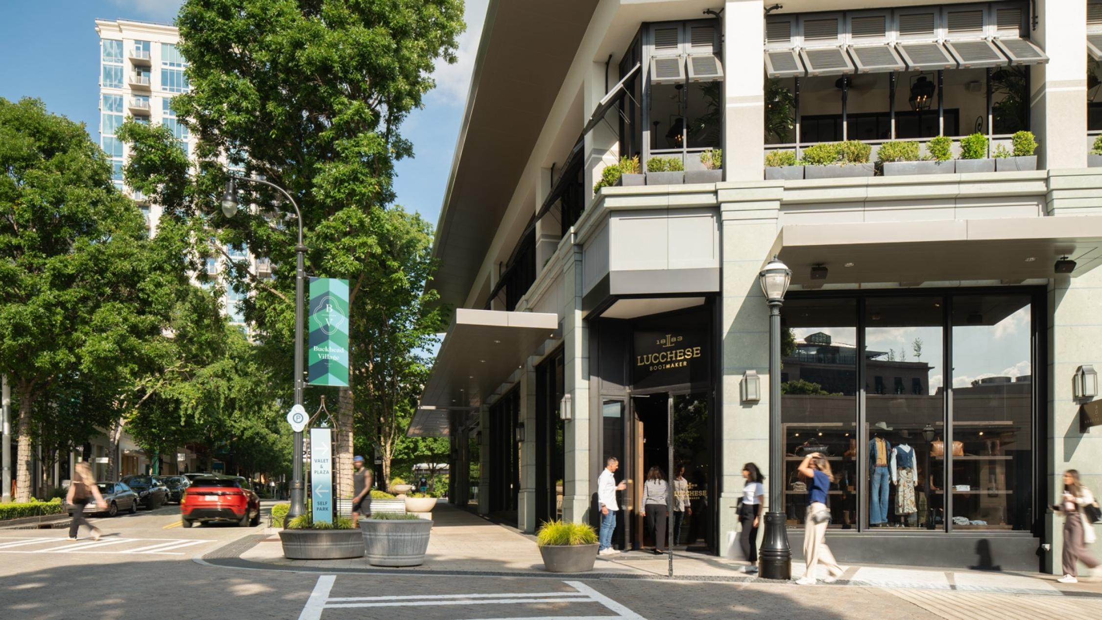 People walking on sidewalks in front of shops and crossing a street at Buckhead Village