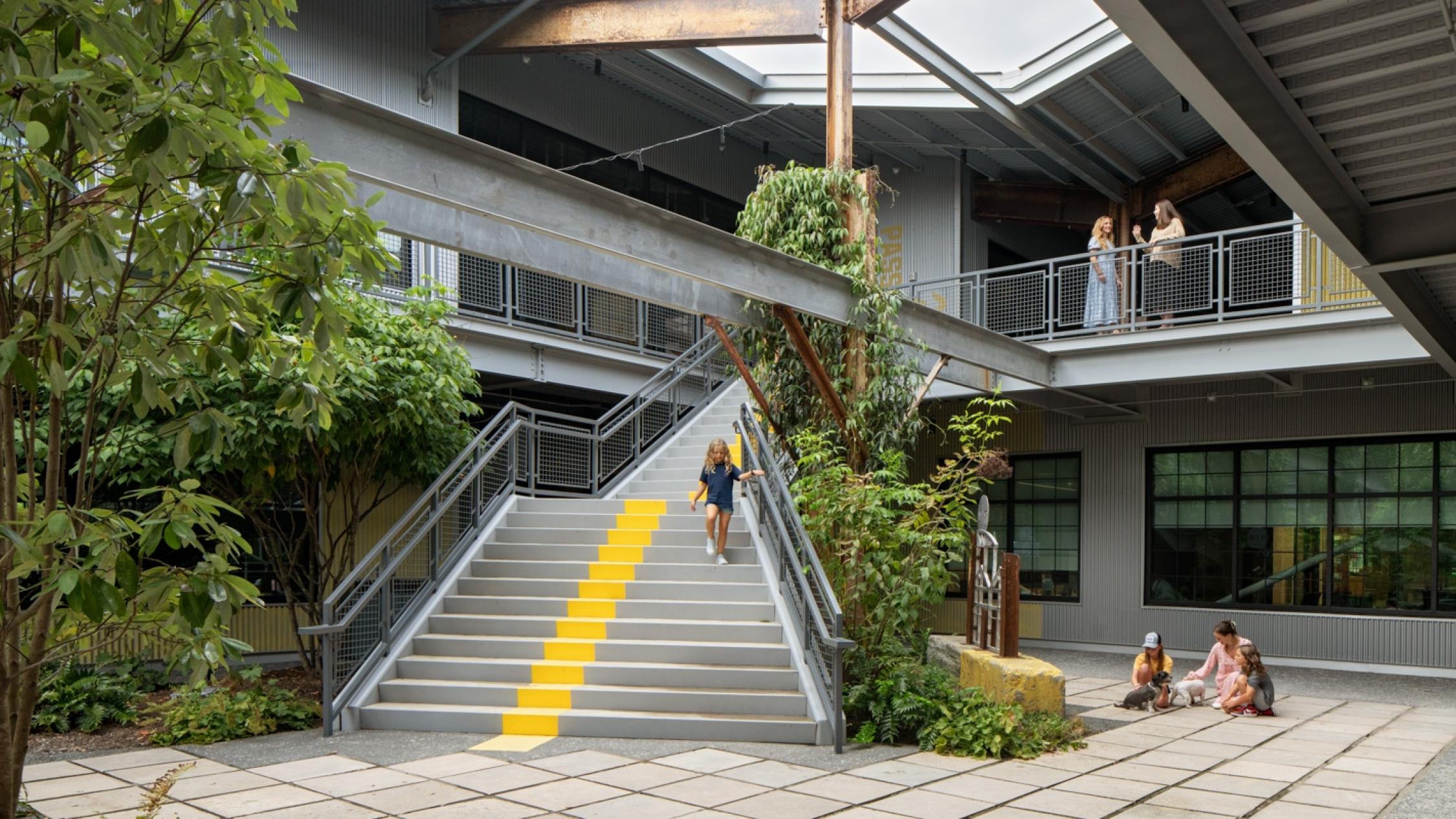 Exterior multi-level courtyard connected by stairwell with visitors sitting and walking at Raleigh Iron Works
