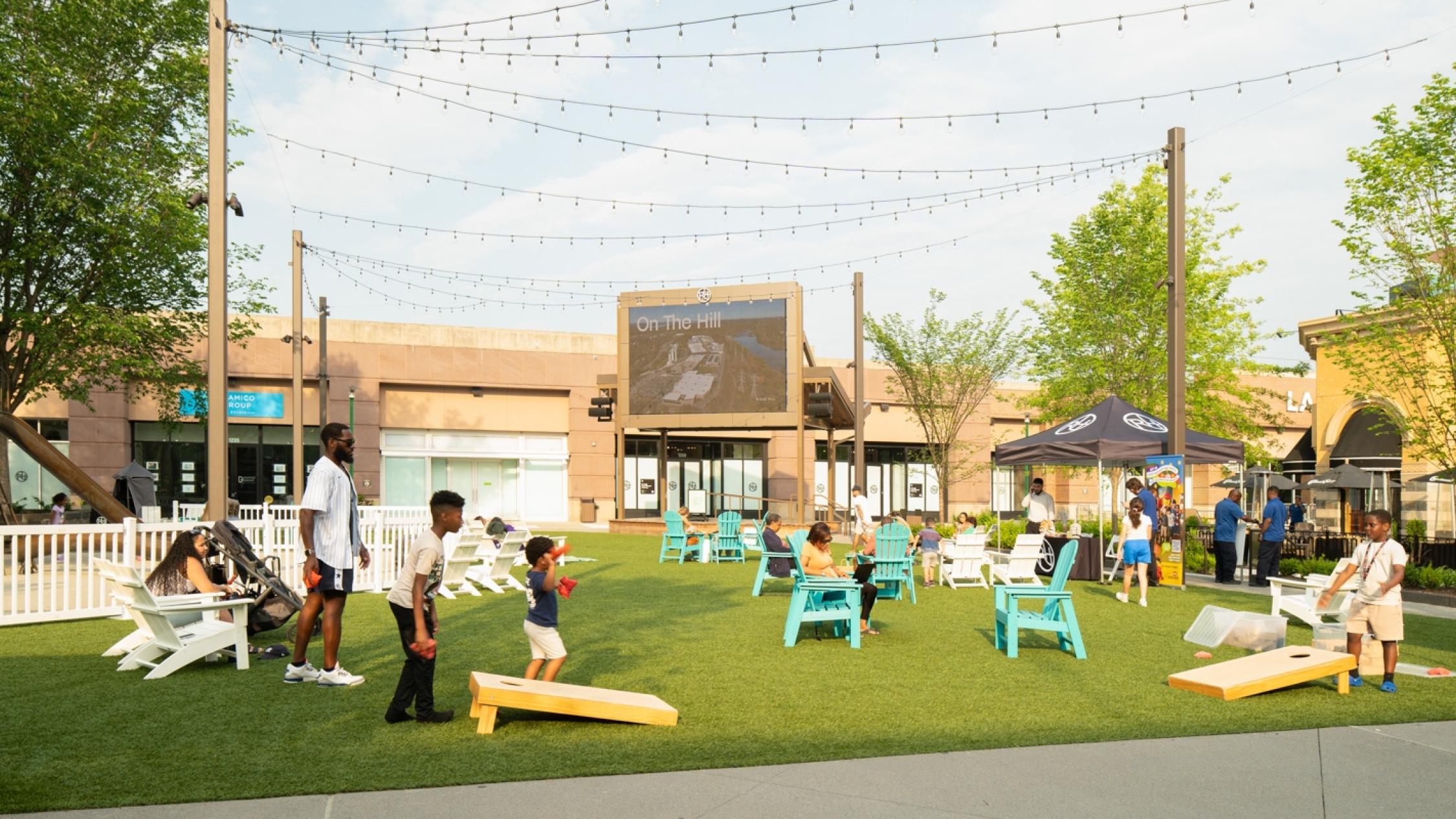 People sitting in Adirondack chairs and playing a cornhole game in an outdoor courtyard at Ridge Hill