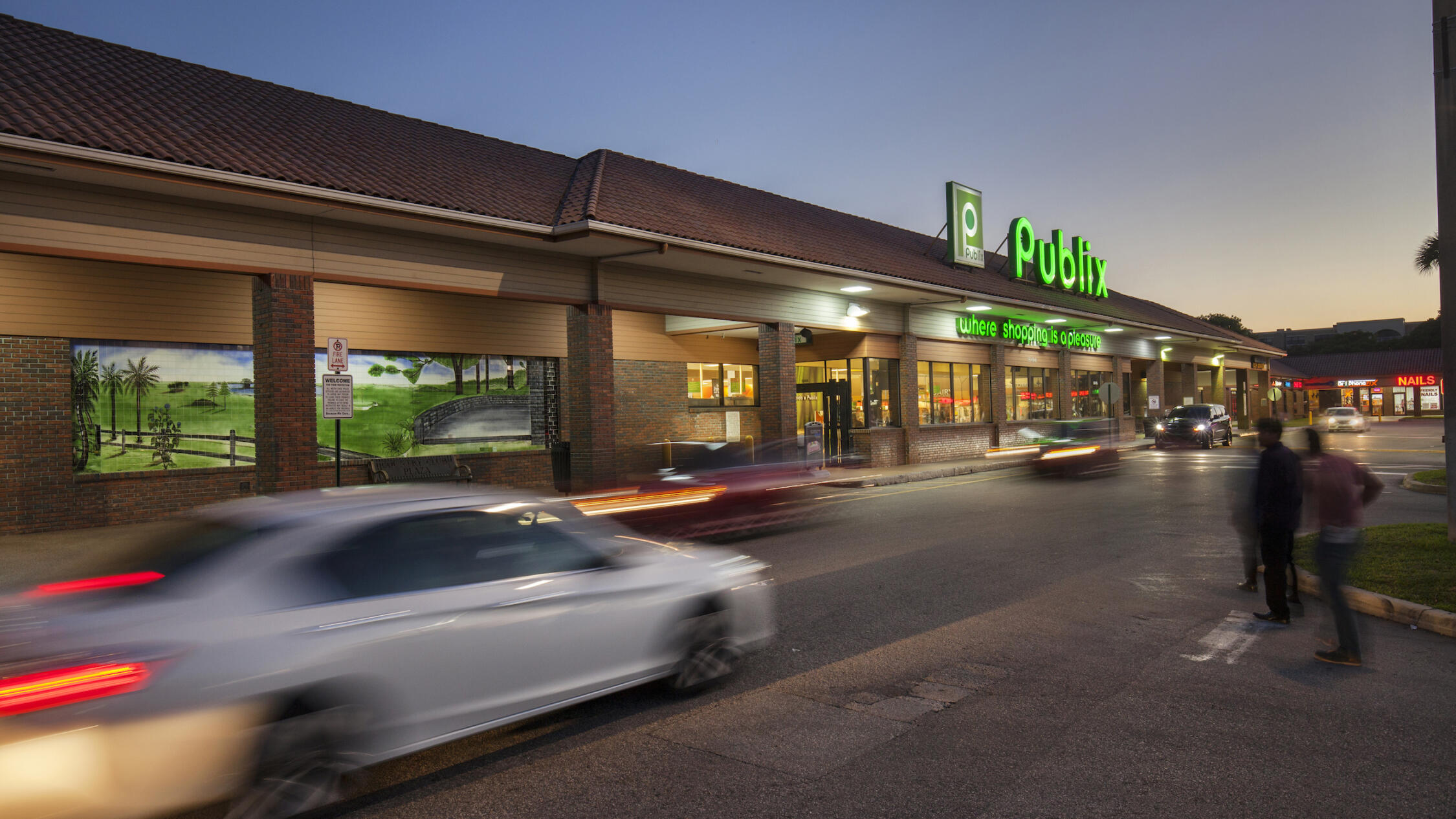 Country Club Plaza exterior of grocery store at dusk with cars and pedestrians in driveway