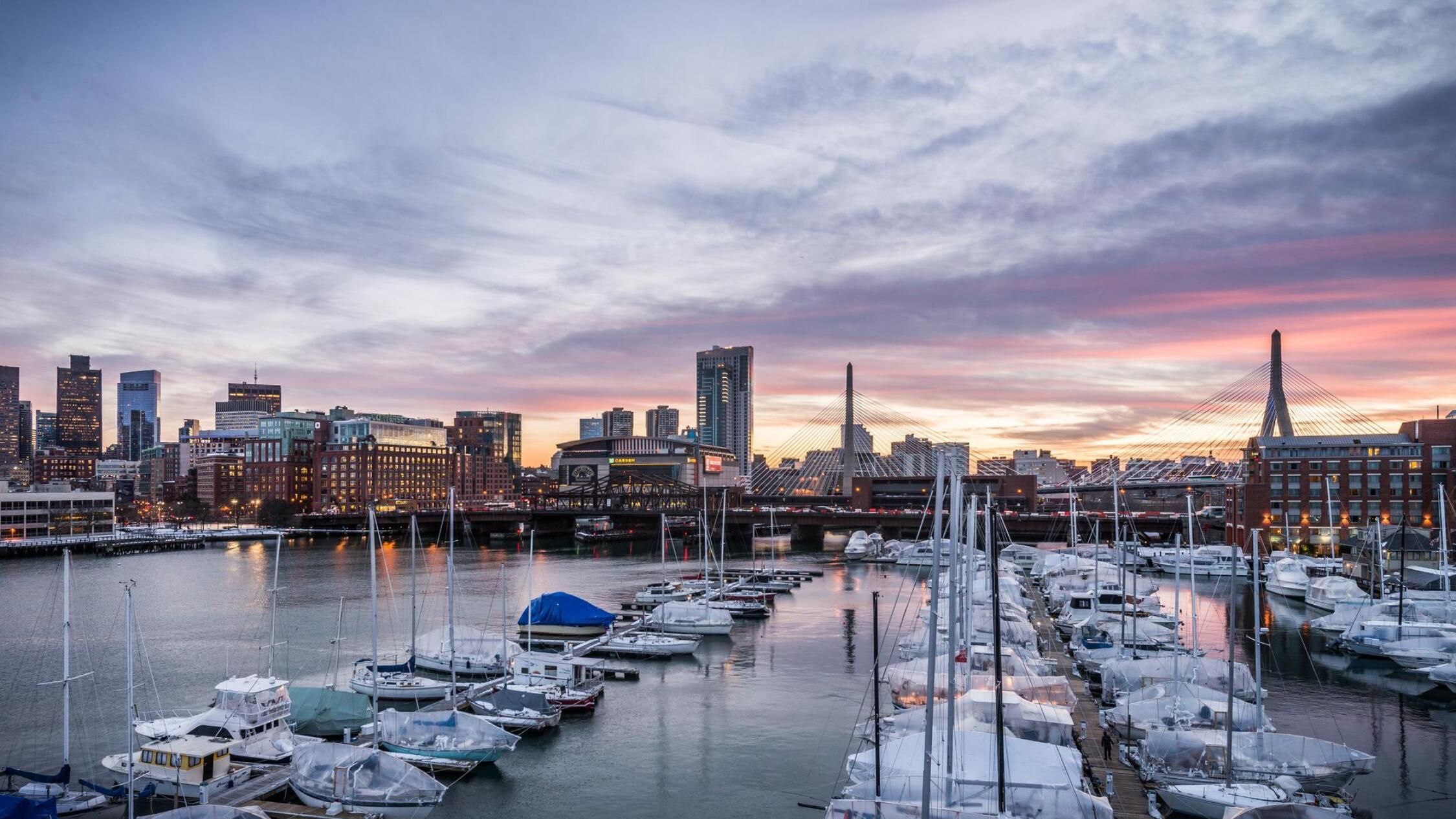 View of moored sailboats at the marina, with the Boston skyline in the background under a beautiful sunset sky