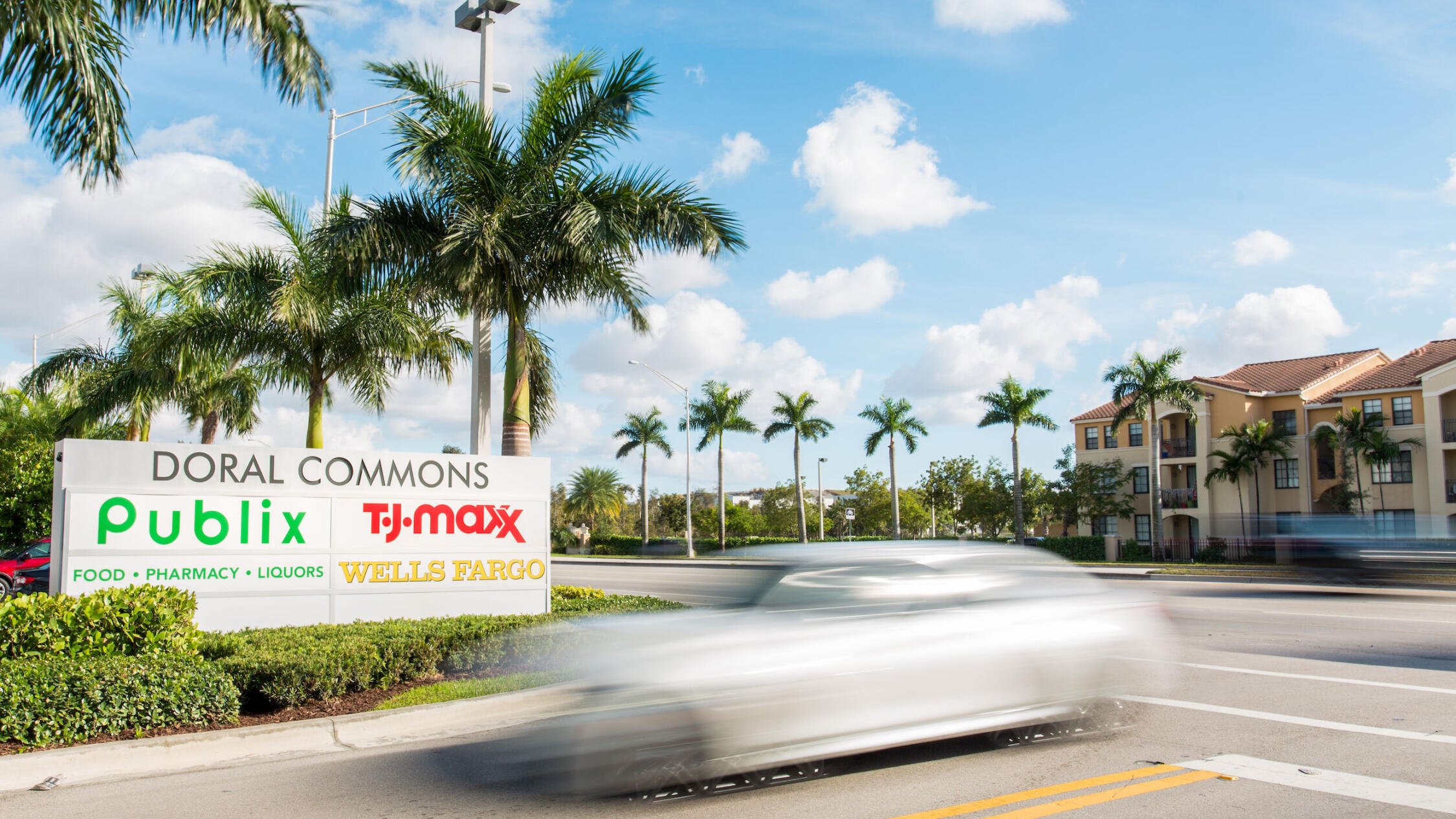 Doral Commons parking lot entrance with monument sign and street lined with palm trees