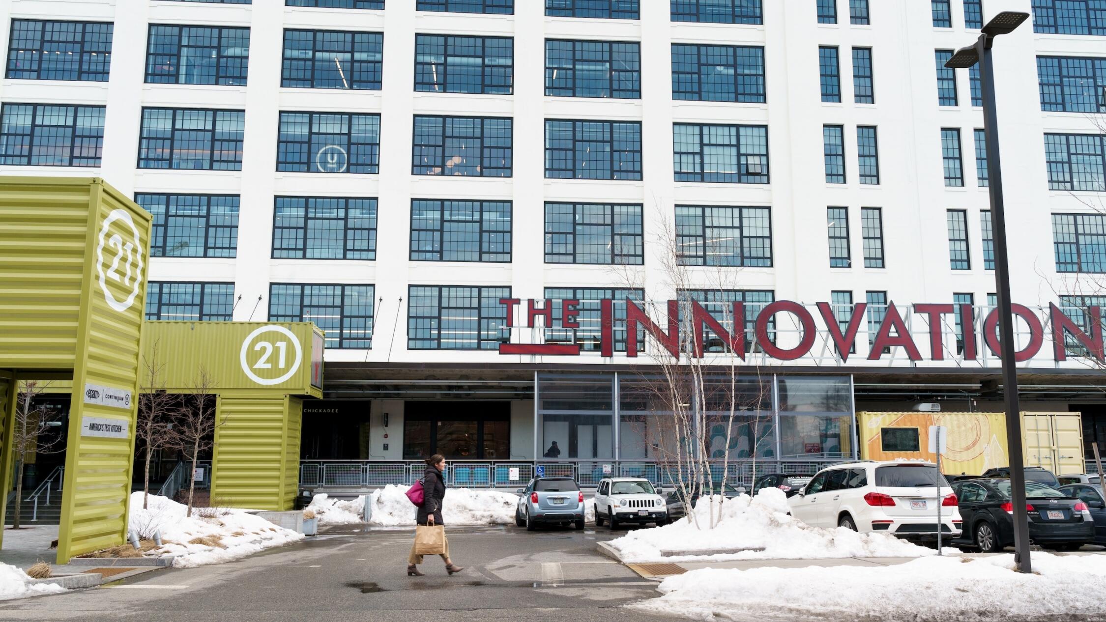 Woman walking with a tote bag in front of The Innovation and Design Building in the wintertime with snow on the ground