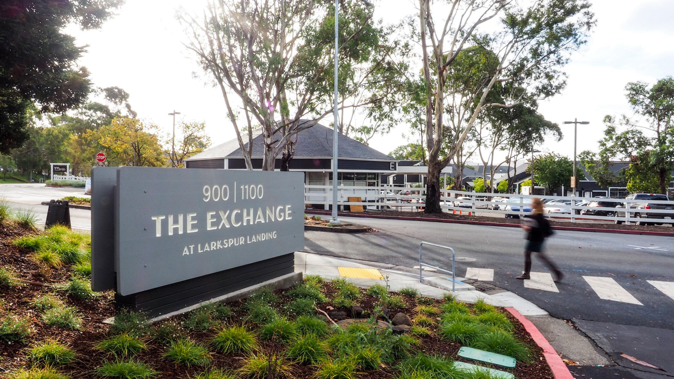 Street signage of The Exchange at Larkspur Landing with a person crossing the road nearby