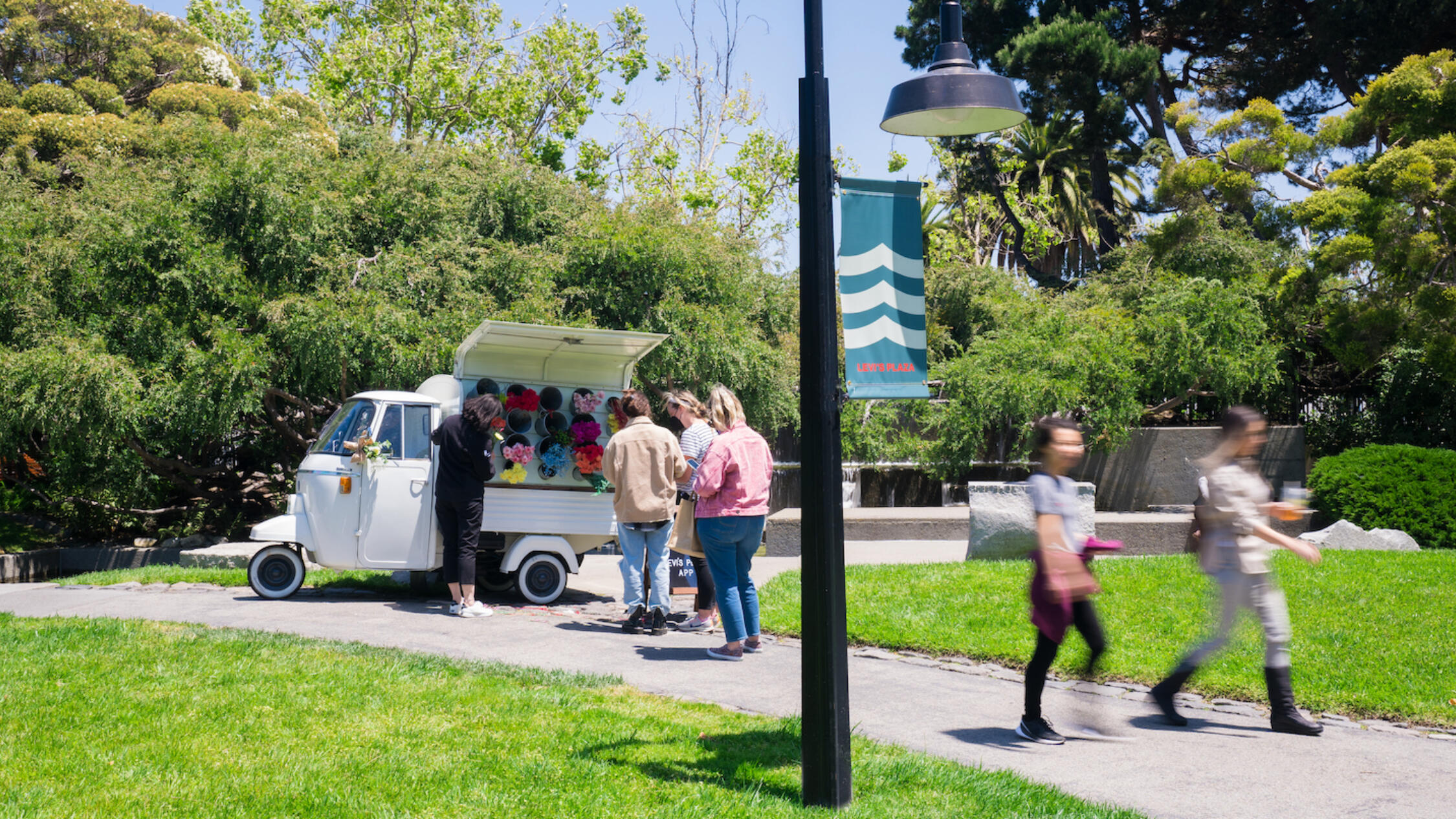 Women walk and buy flowers at a stand outside Levi's Plaza