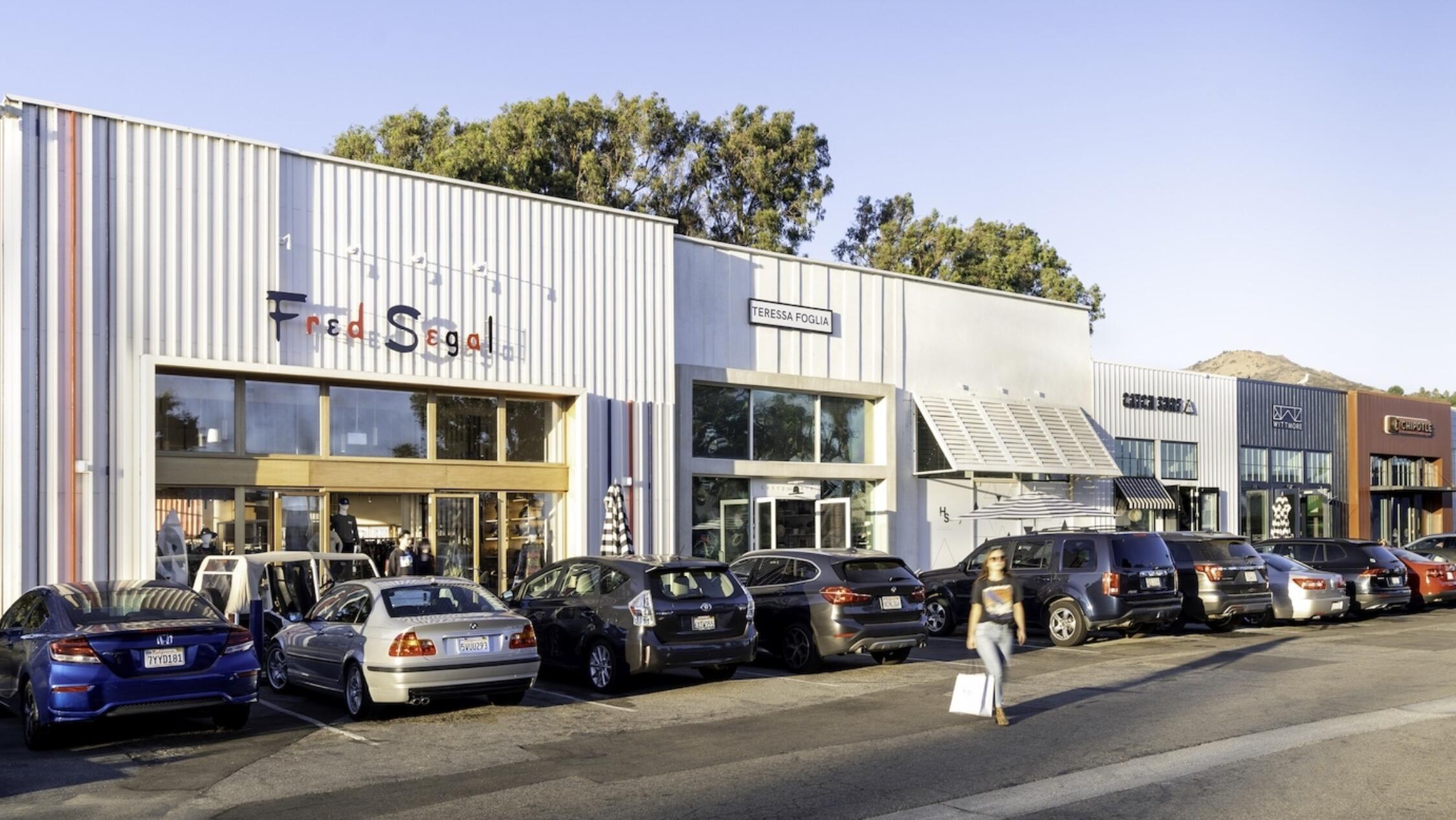 Exterior of Fred Segal at Malibu Village with shopper walking near cars parked in lot
