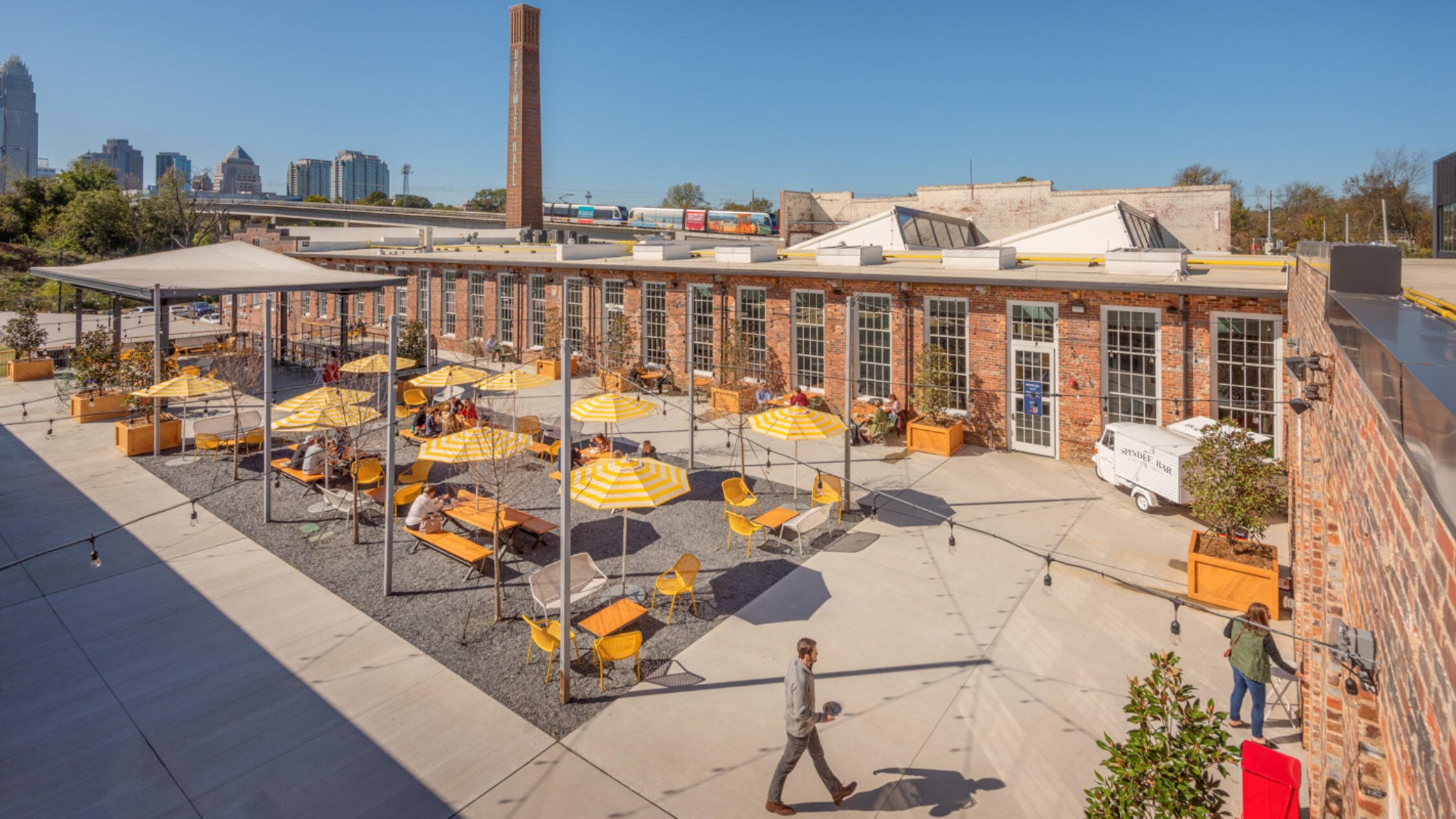 Optimist Hall outdoor courtyard with tables and chairs under umbrellas and skyline in background