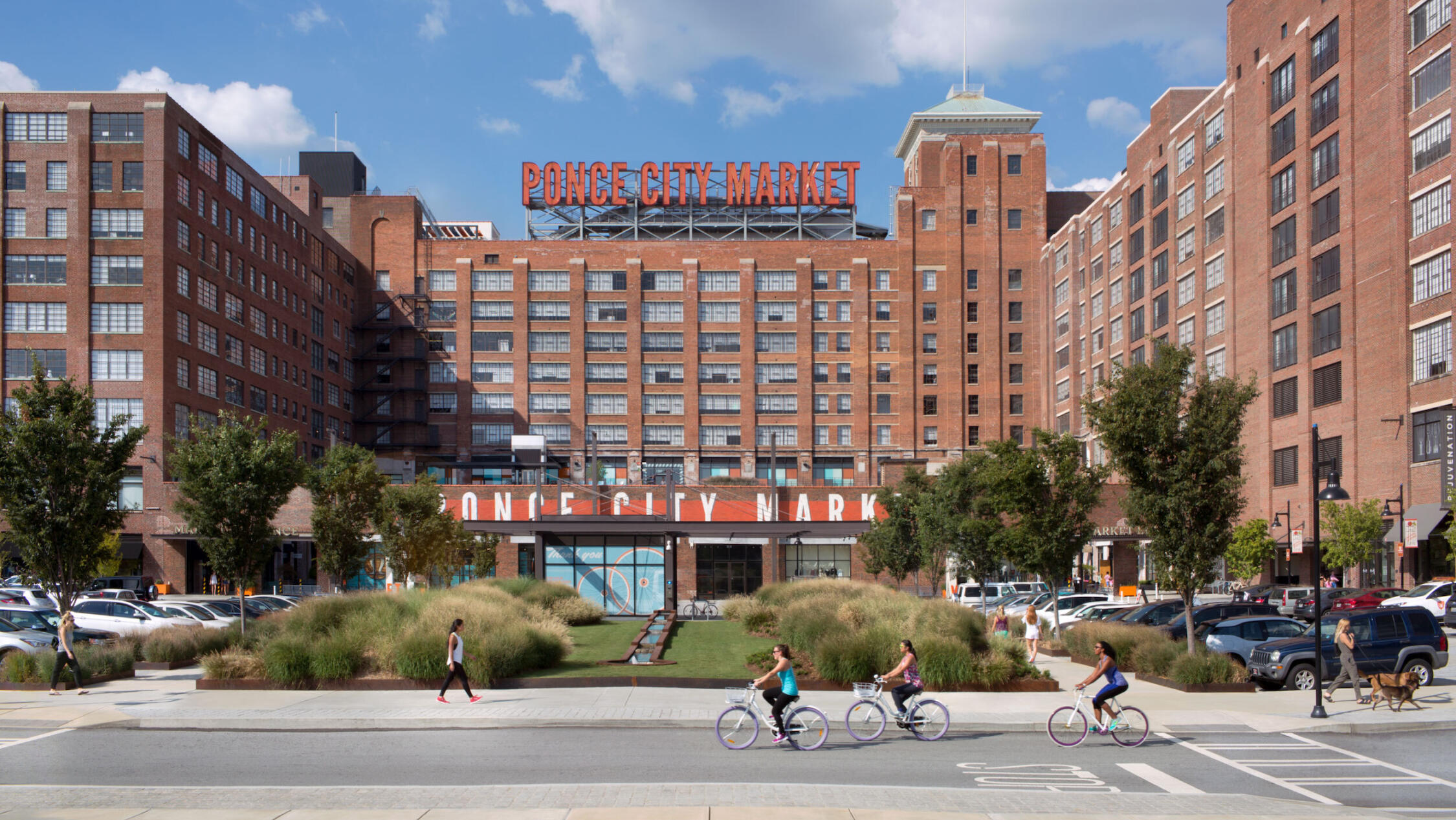 Cyclists pass by Ponce City Market under a blue sky