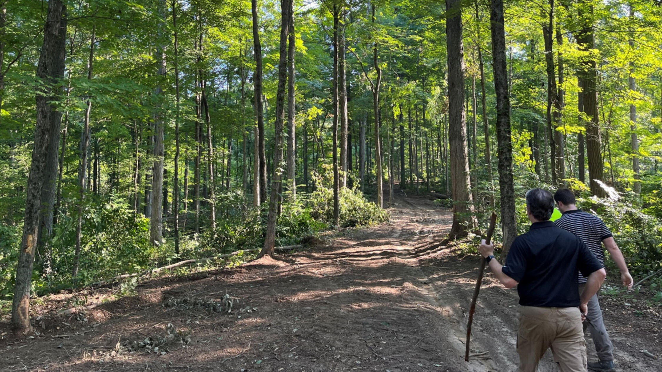 Two foresters hiking on dirt path beneath trees at Brickyard