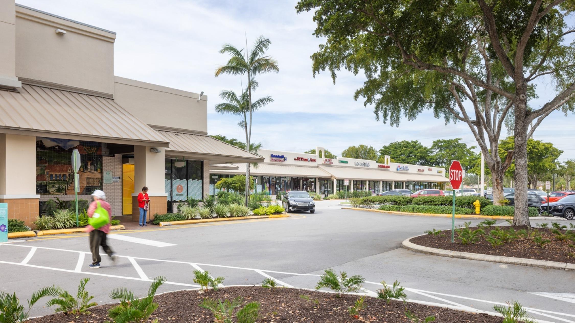 Various store exterior facades with a pedestrian in the driveway at Cypress Commons