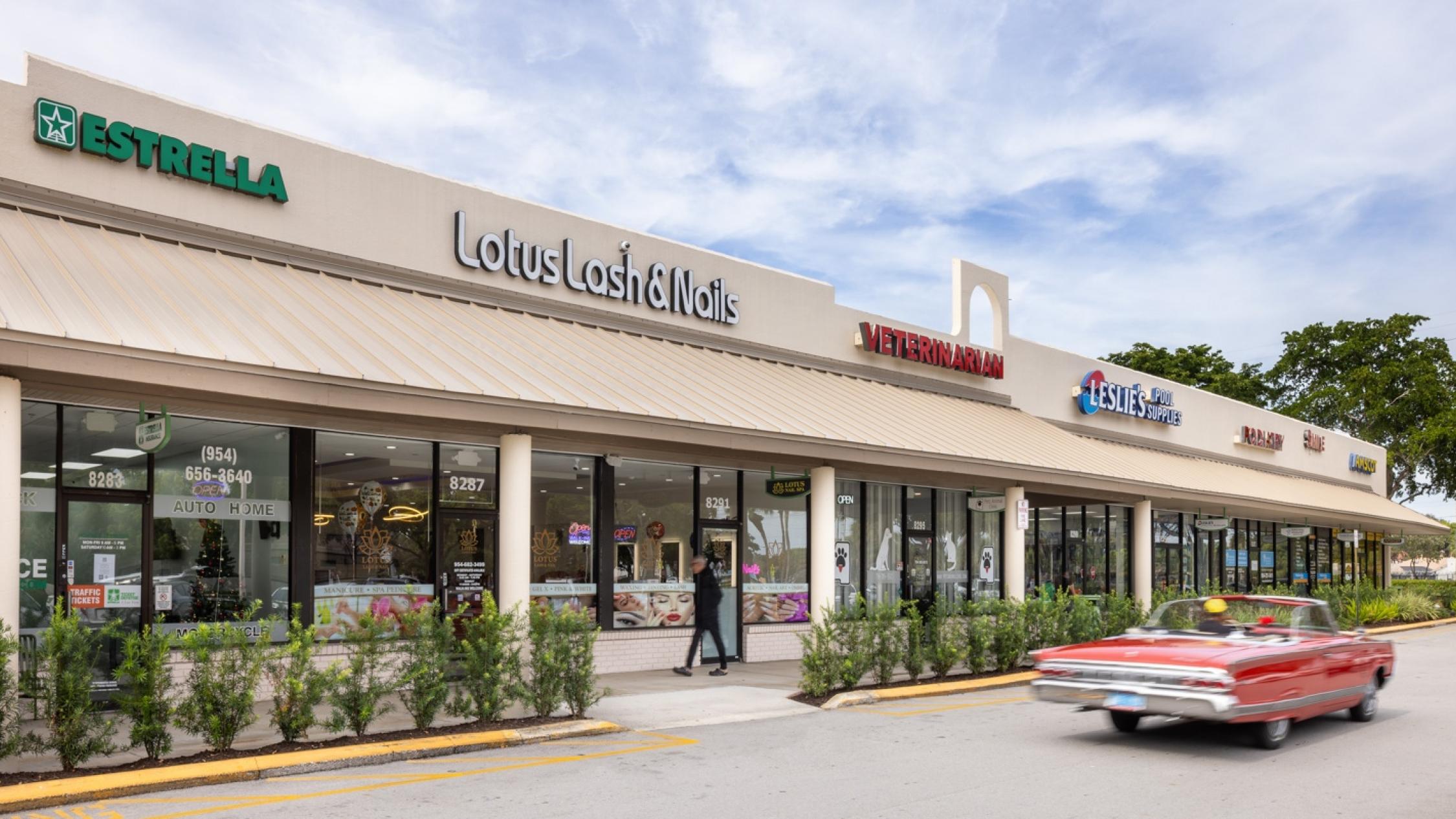 Various store facades with a pedestrian on the sidewalk and classic car in the driveway at Cypress Commons
