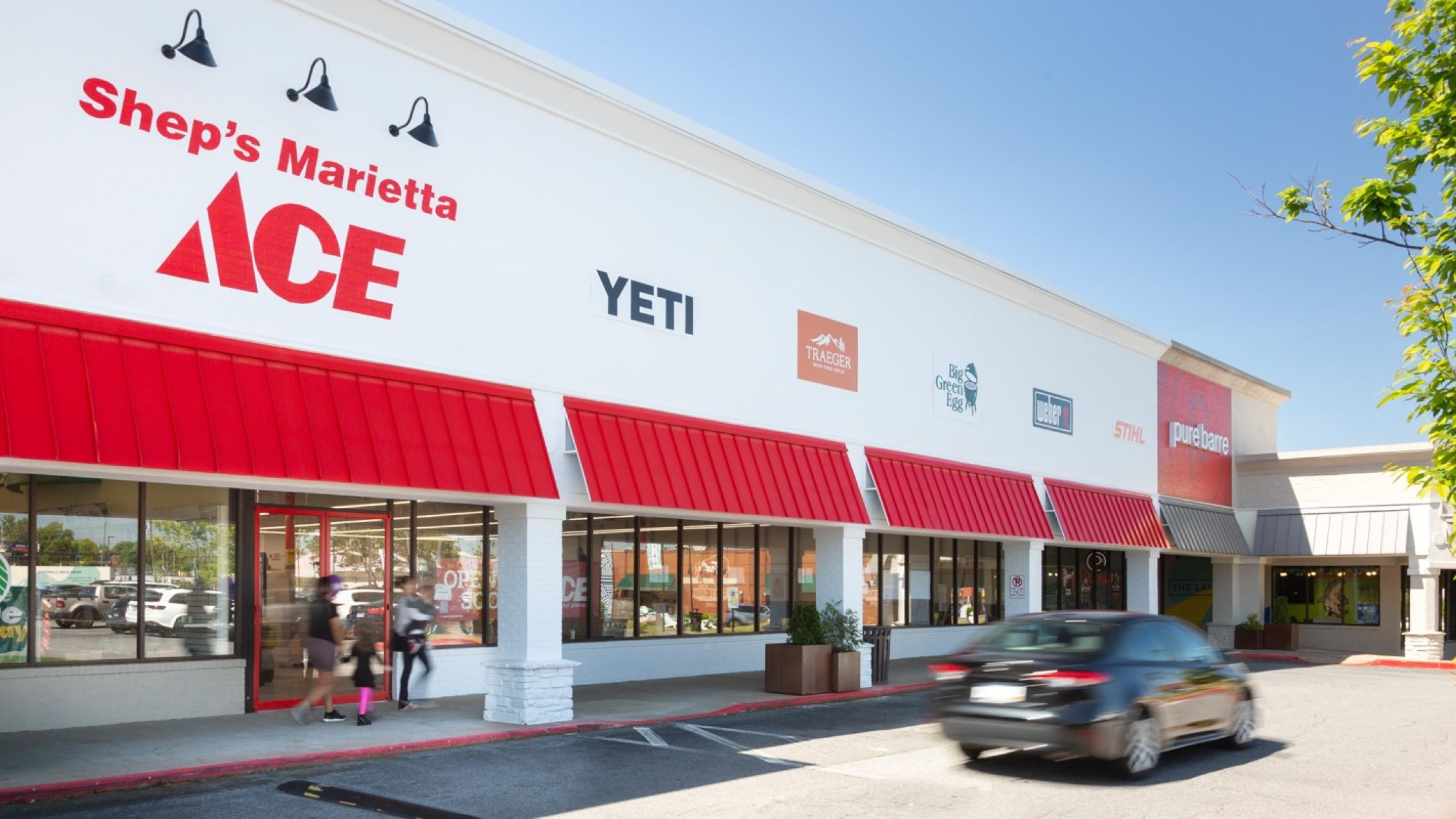 Various store exterior facades with pedestrians on sidewalk and car in driveway at Parkaire Landing