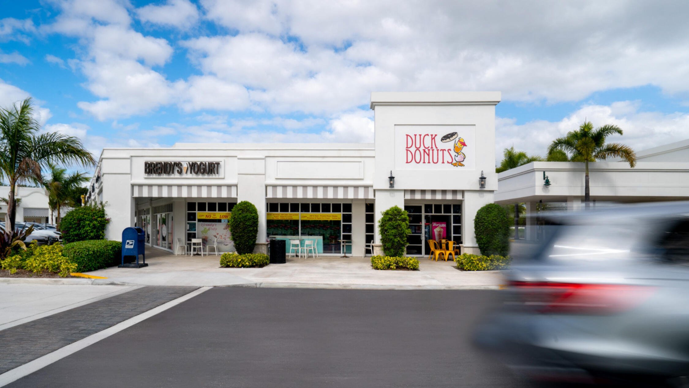 Brendy's Yogurt and Duck Donuts store facades at Polo Club Shops, with car moving across the parking lot