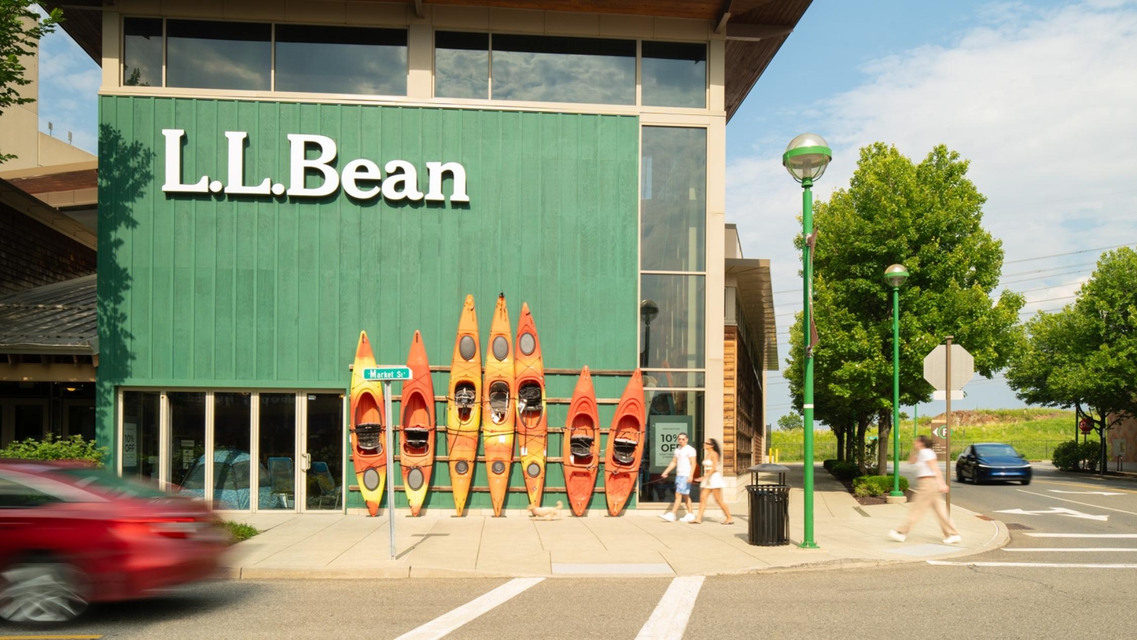 Visitors walking on a sidewalk in front of shop that's displaying orange kayaks at Ridge Hill