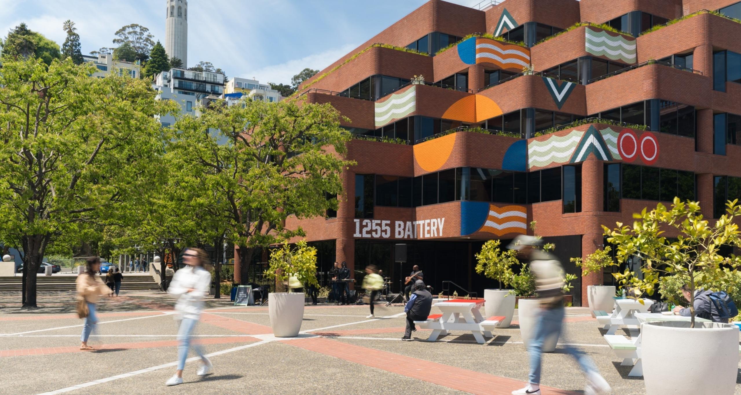 People walking around an outdoor courtyard at Levi's Plaza, with Coit Tower in background