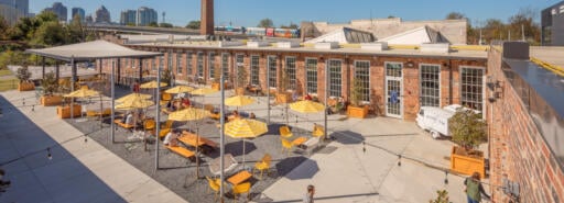 Optimist Hall outdoor courtyard with tables and chairs under umbrellas and skyline in background