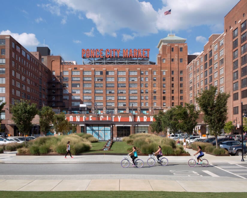 Cyclists pass by Ponce City Market under a blue sky