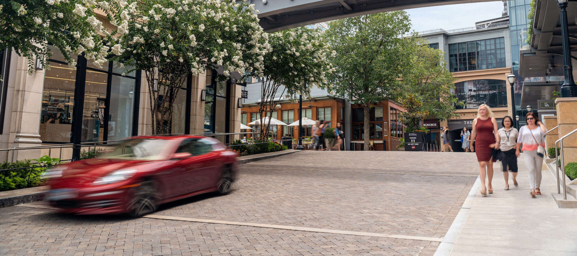 Entrance to The Shops Buckhead Atlanta where people are walking on the sidewalk and a car is passing by