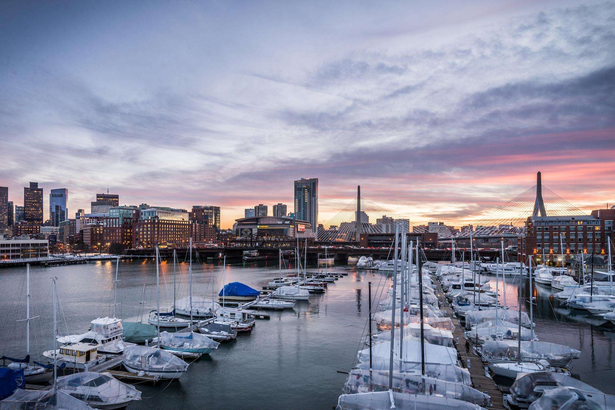 View of moored sailboats at the marina, with the Boston skyline in the background under a beautiful sunset sky