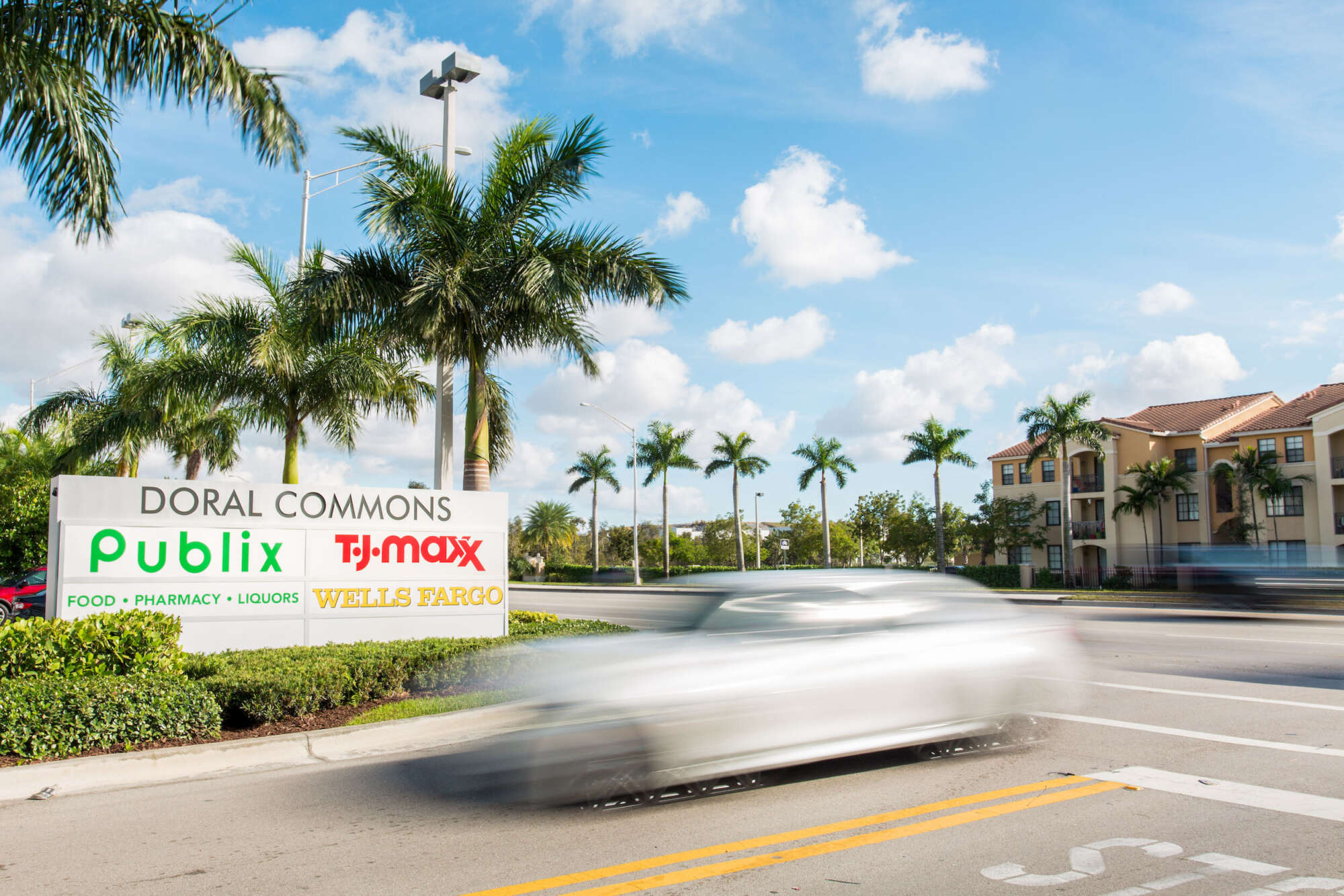 Doral Commons parking lot entrance with monument sign and street lined with palm trees