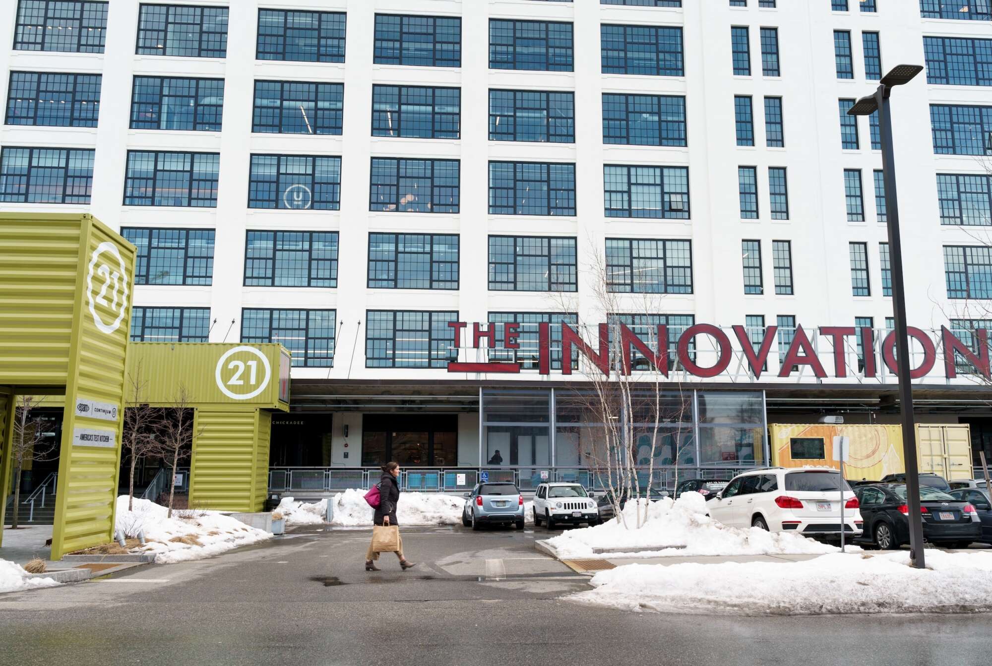 Woman walking with a tote bag in front of The Innovation and Design Building in the wintertime with snow on the ground