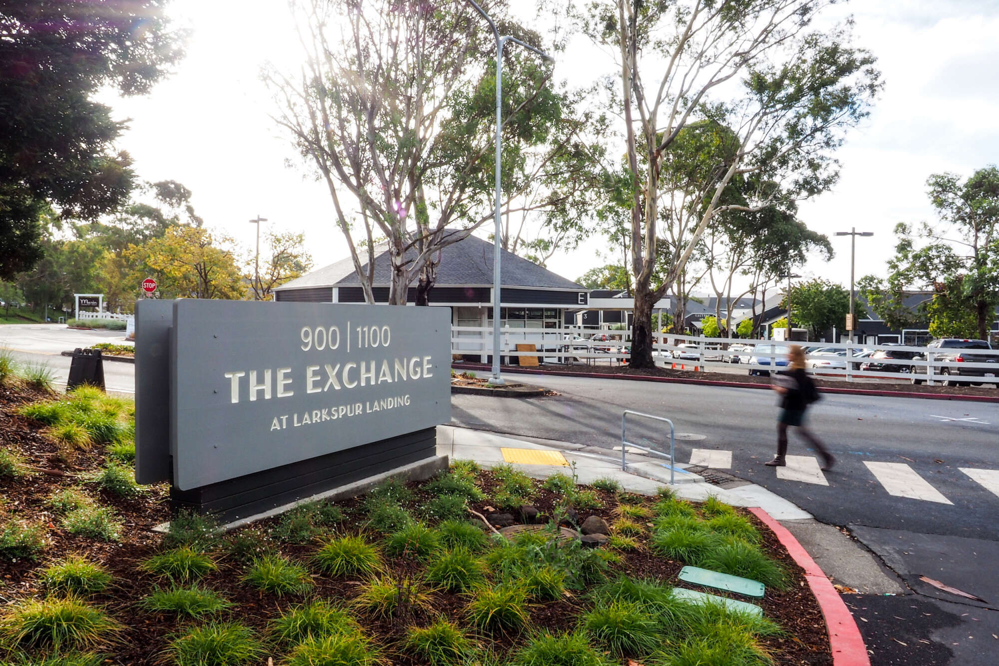Street signage of The Exchange at Larkspur Landing with a person crossing the road nearby
