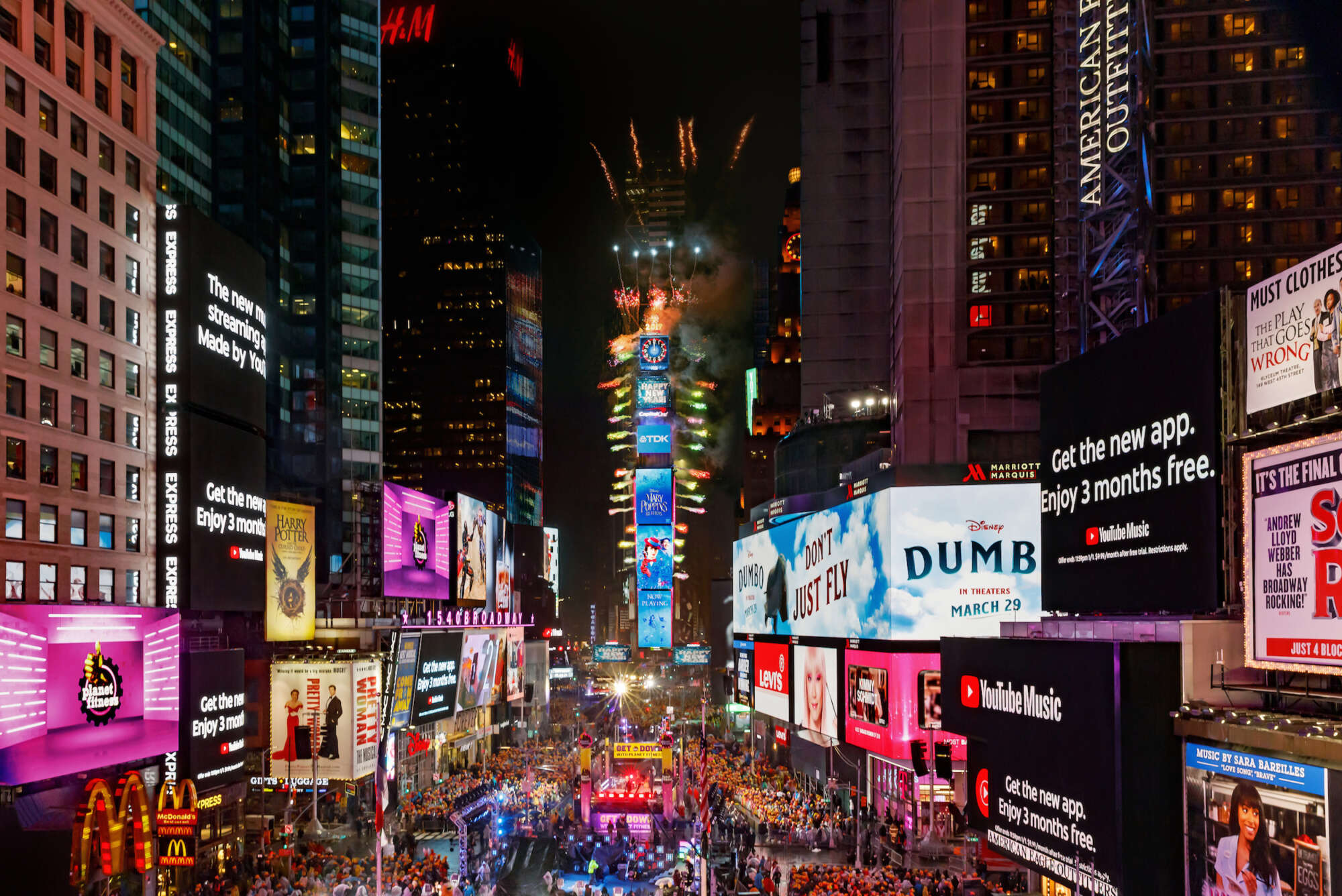 One Times Square at New Years with people in the crowd below and fireworks exploding from the building.