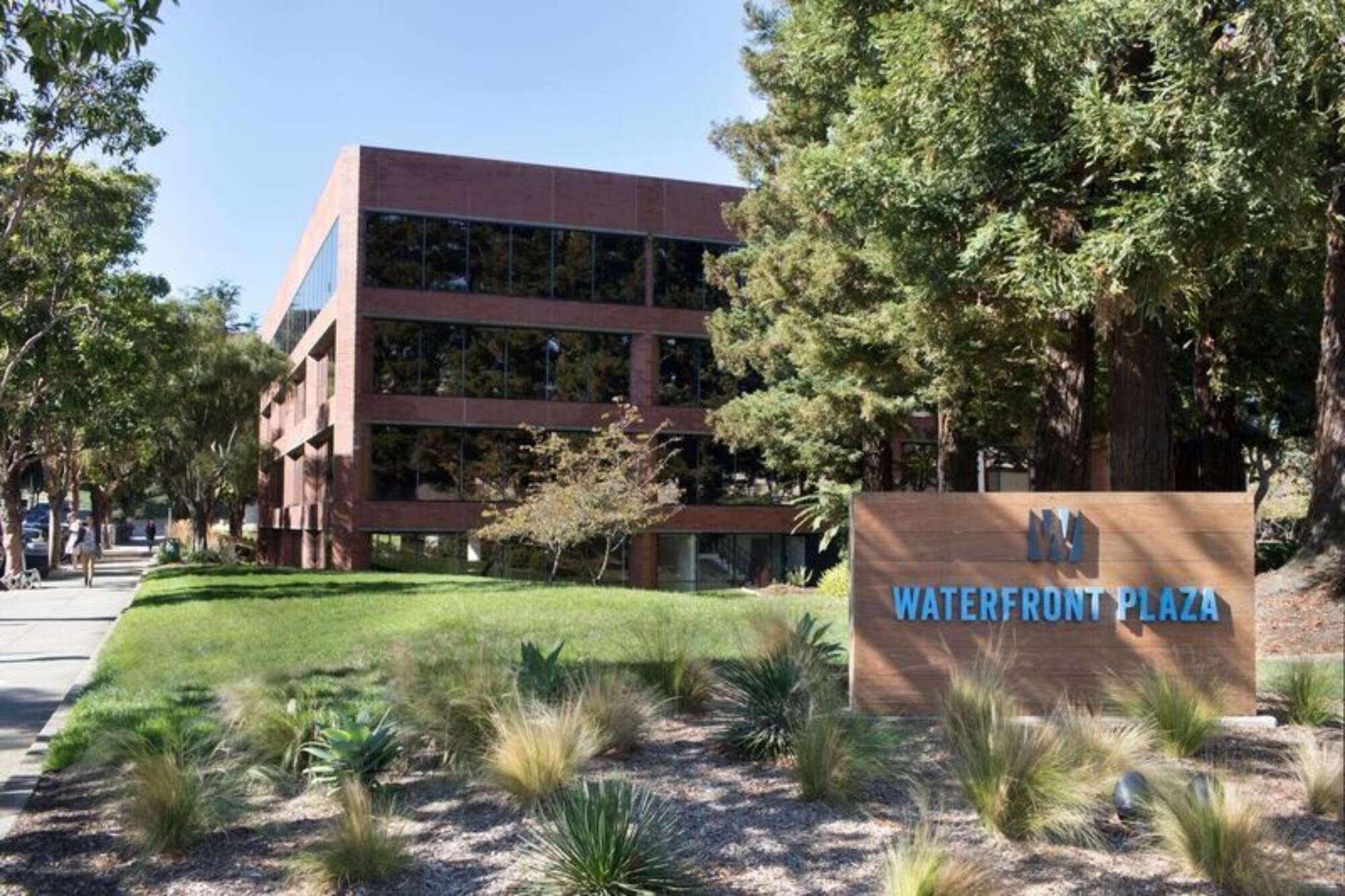 Exterior of The Waterfront Collection with green grass and lush trees under a clear sky